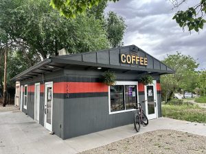 Small gray coffee shop with a red stripe, bicycle parked by the window, under a cloudy sky at Arches National Park.
