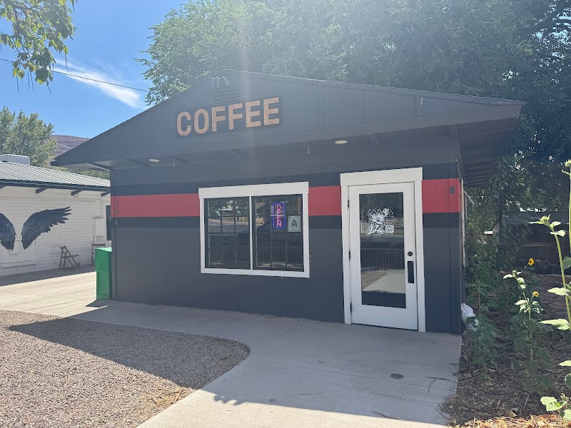 Small dark gray cafe building with a red stripe, a large COFFEE sign on the roof, white-framed window and door in Arches National Park.