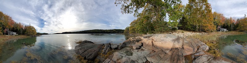 Deer Isle shoreline at Acadia National Park featuring rocky coast, calm water, and autumn foliage.