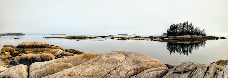 Deer Isle coastline in Acadia National Park, with a rocky shoreline and a small forested island reflected in calm water.
