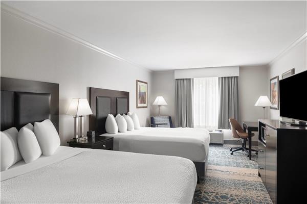 Two queen beds with white linens, bedside lamps, seating area, desk, flatscreen TV in a hotel room at Arches National Park.