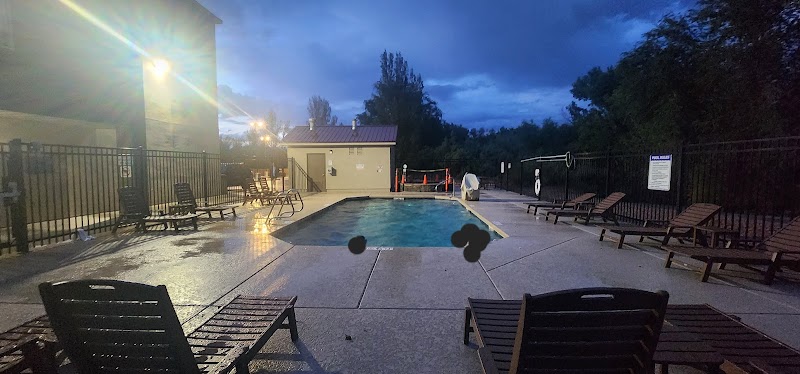 Dusk view of a hotel pool area with wet deck, wooden lounge chairs, and a fenced perimeter in Arches National Park.