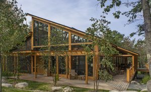 Wood-framed lodge with full-height glass walls and a covered deck, surrounded by trees at Acadia National Park.