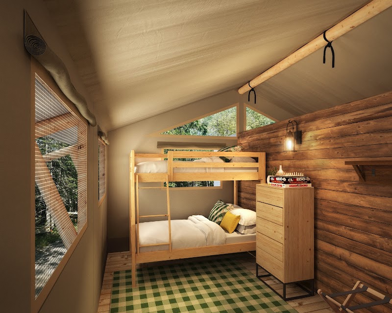 Cozy loft bedroom in a wooden cabin with bunk beds, a dresser, a green checkered rug, warm lighting, and large windows in Acadia National Park.