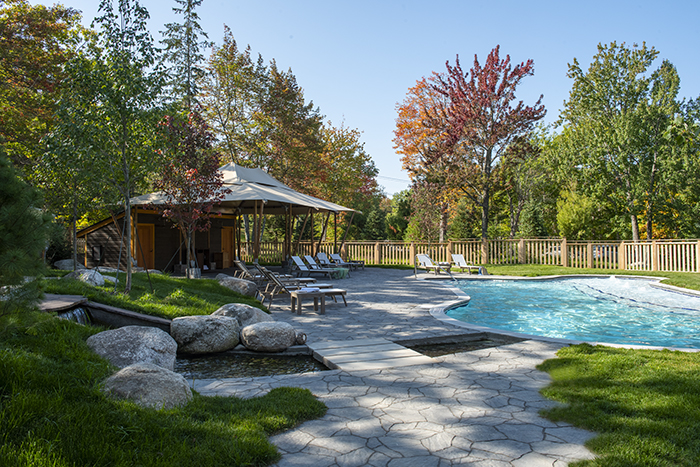 Poolside view of a lodge with a shaded pavilion, lounge chairs, and a stone patio in Acadia National Park.