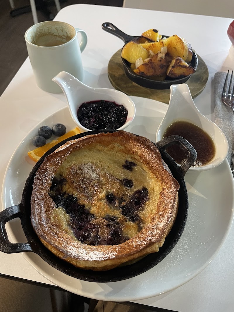 Acadia National Park breakfast featuring a blueberry pancake in a cast-iron skillet with blueberry compote, roasted potatoes, and syrup.