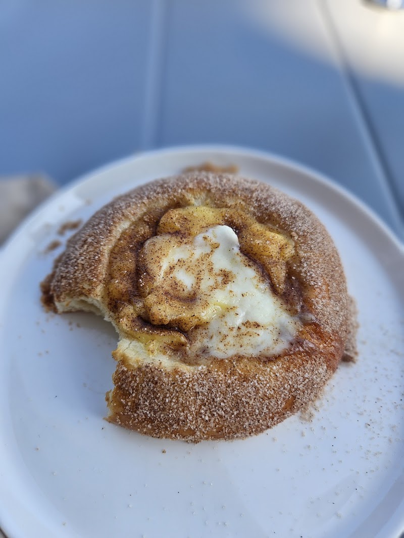 Cinnamon roll with cream cheese frosting and sugar dusting on a white plate at a blue table in Acadia National Park.