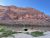 Red sandstone cliffs rise over a calm riverbank with two camping chairs on the shore, Arches National Park.