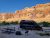 Dark camper van beside a picnic table and campfire ring, with folding chairs, in Arches National Park cliffs.