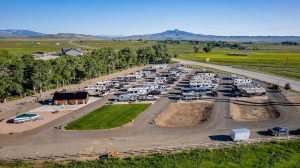 RV campground in Yellowstone National Park with rows of trailers and RVs arranged on gravel lots amid green fields and distant mountains.