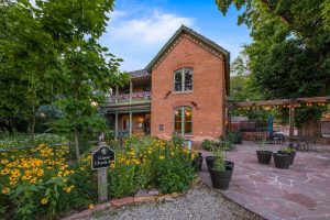 Brick lodge with string lights, stone-patio courtyard, potted plants, yellow flowers, and a guest check-in sign at Arches National Park.