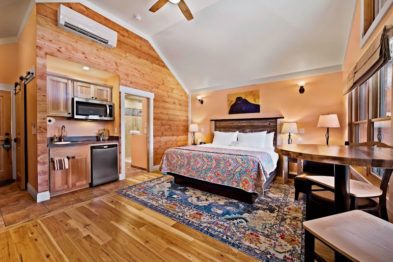 Cozy hotel room with king bed, colorful quilt, wood-paneled walls, kitchenette, desk, and window in Arches National Park.