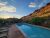 Poolside lounge chairs and blue umbrellas overlook a reflecting pool with red rock cliffs of Arches National Park.