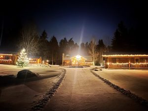Snowy Somers Bay log cabins glow warmly at night, with festive lights guiding visitors in Glacier National Park.