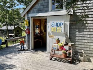 Gift shop in Acadia National Park sits on a wooden deck with jars, flowers, and a blue SHOP sign.