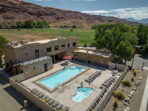 Beige lodge complex with two pools and many loungers, framed by red rock cliffs at Arches National Park.