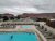 Poolside with lounge chairs around a fenced courtyard, as rugged red rock cliffs of Arches National Park loom beyond RVs and buildings.
