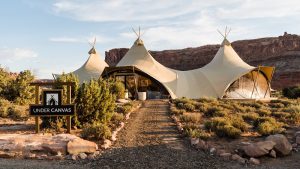 Wide view of a beige canvas lodge with three peak tents along a gravel path, in Arches National Park.