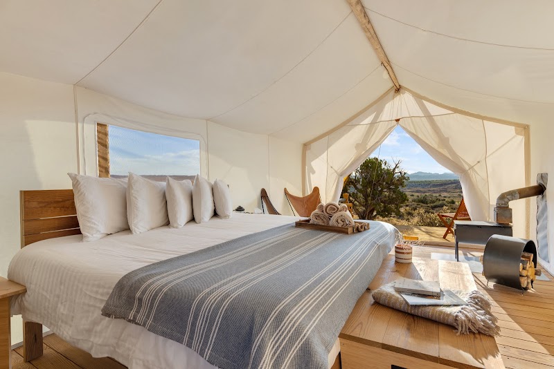 Lux glamping tent interior at Arches National Park with a king bed, white linens, striped throw, and desert views.