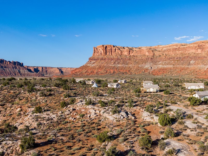 Desert campground with white canvas tents dotting the rocky terrain beneath red mesas in Arches National Park.