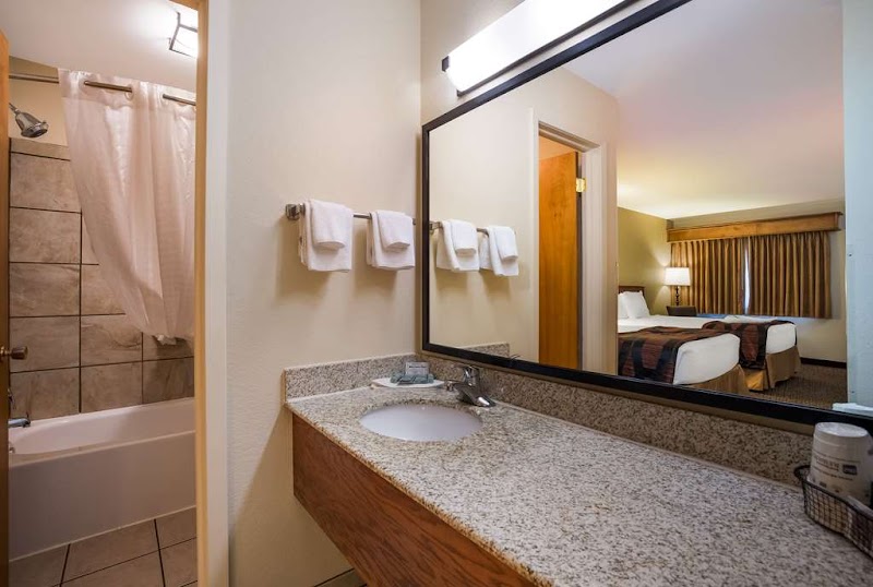 Hotel bathroom with granite counter and single sink, large mirror, towels on a rack, and a view into a twin‑bed room at Badlands National Park.