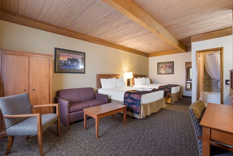 Spacious hotel room in Badlands National Park with two queen beds, a seating area, wooden beams, and warm lighting.