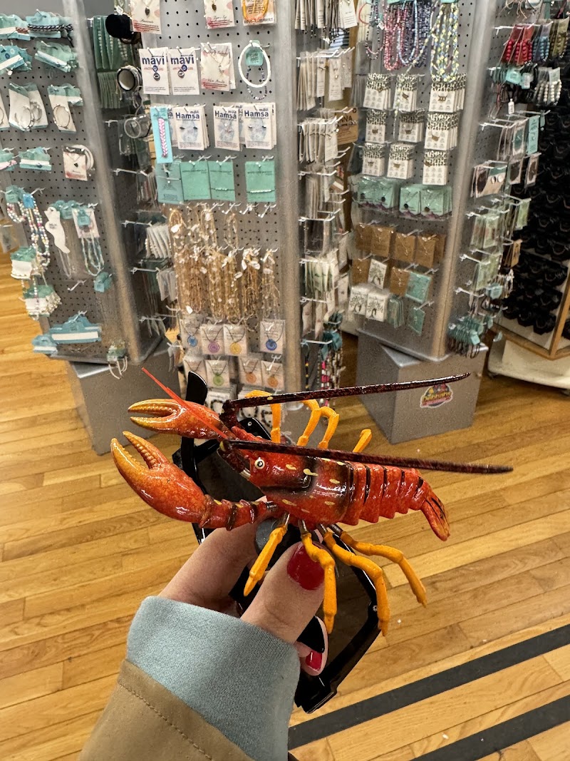 Shoppers' hand holds a bright red lobster figurine in front of jewelry and trinket displays inside Acadia National Park gift shop.