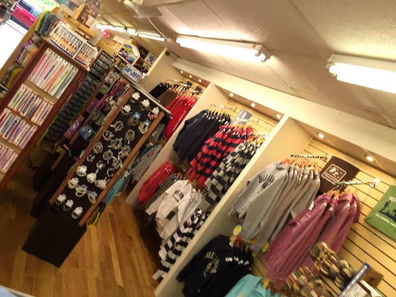 Inside a gift shop at Acadia National Park, clothing racks hold striped sweaters, hoodies, tees, and shelves of souvenirs.