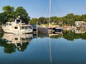 Harbor scene in Acadia National Park with docked motor yacht and sailboats, calm water reflecting trees and boats.