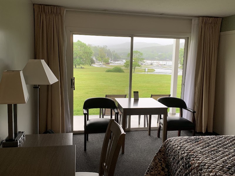 Hotel room with sliding glass doors opening to a green lawn and marina, a table and chairs, and a patterned bed in Acadia National Park.
