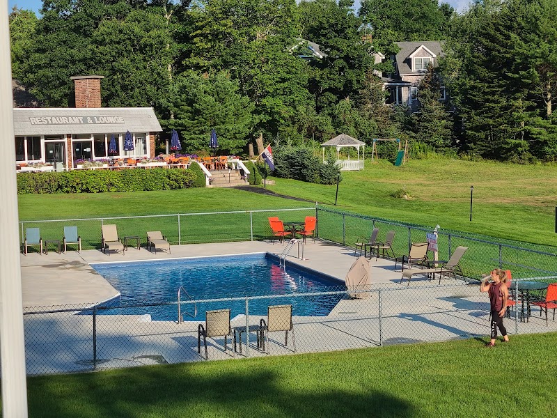 Outdoor pool area at Acadia National Park with lounge chairs, a fenced pool, and a gray cafe building in the background.