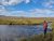 A man stands at the edge of a shallow creek near Indian Creek Campground in Yellowstone National Park under a bright blue sky.