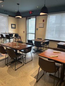 Cozy dining area with wooden tables and black chairs, napkins set at each, pendant lights, and large windows in Acadia National Park.