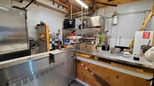 Busy takeout kitchen in Acadia National Park with stainless steel counters, ovens, shelves, and staff at work.