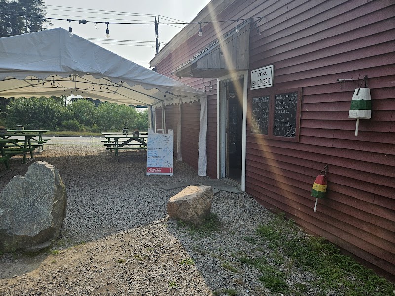 Red wooden outpost with chalkboard menu under a white canopy, gravel yard, picnic tables, and painted buoys at Acadia National Park.