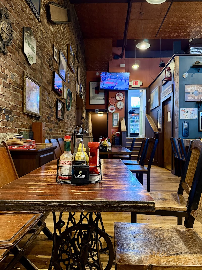 Cozy brick-walled pub interior in Acadia National Park with a long wooden table, condiment caddy, wall TVs, and stairs to a back room.