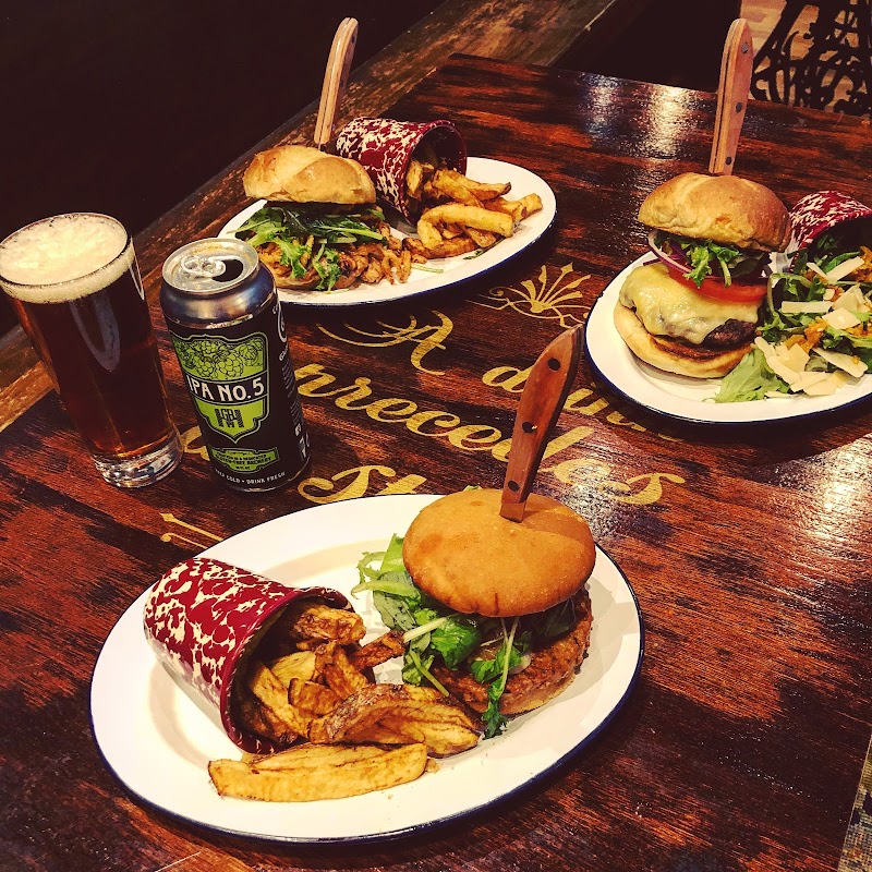 Three burgers with fries and greens on a dark wooden table, plus a beer and a can, in Acadia National Park.