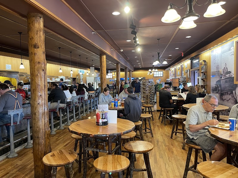 Busy Yellowstone National Park gift shop dining area with round wooden tables, tall posts, and a long counter full of customers.