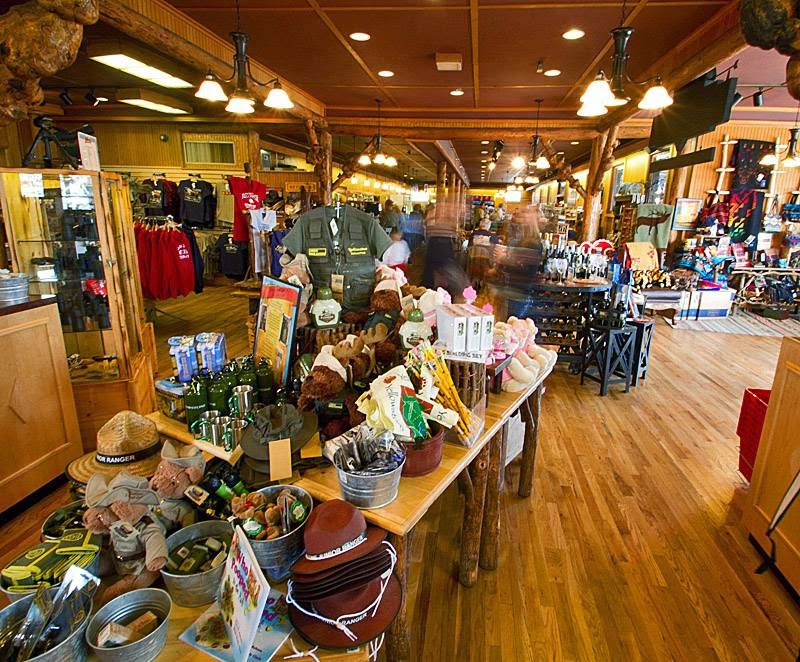 Cozy Yellowstone National Park gift shop interior with wooden beams, racks of shirts, hats, mugs, and souvenirs.