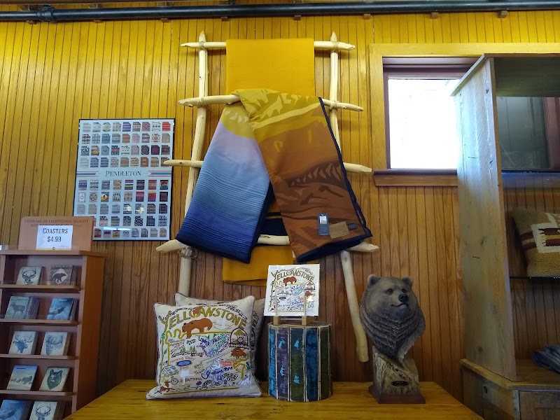 Inside a Yellowstone National Park gift shop, yellow paneled walls display woven blankets, a bear statue, and Yellowstone pillows.