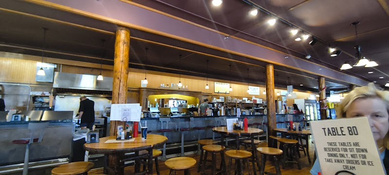 Inside a Yellowstone National Park gift shop with wooden columns, round tables and stools, a long service counter, and customers browsing.