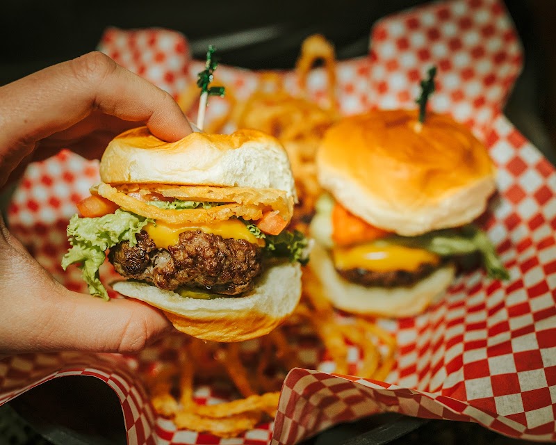 A hand holds a cheeseburger slider with lettuce and tomato beside fries in a red-checkered basket at Badlands National Park.