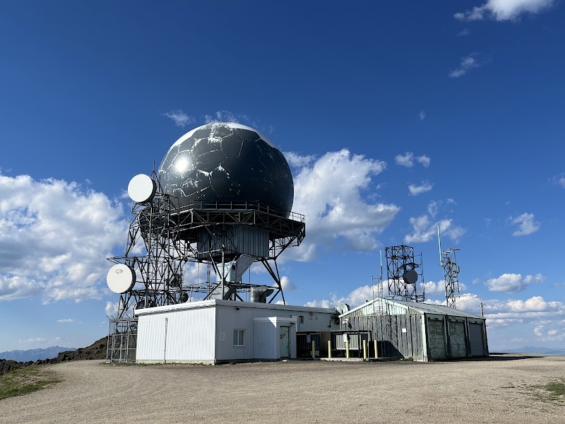 Large radar dome on a metal lattice with satellite dishes and white utility buildings in Yellowstone National Park.