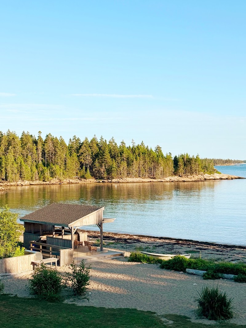 Goose Cove Beach pavilion at Acadia National Park sits beside calm water with pine trees lining the shore.