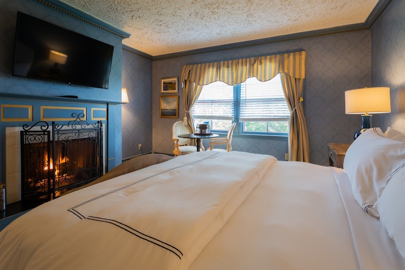 Cozy hotel room in Acadia National Park with a lit fireplace, white bedding, blue walls, and a windowed seating area.
