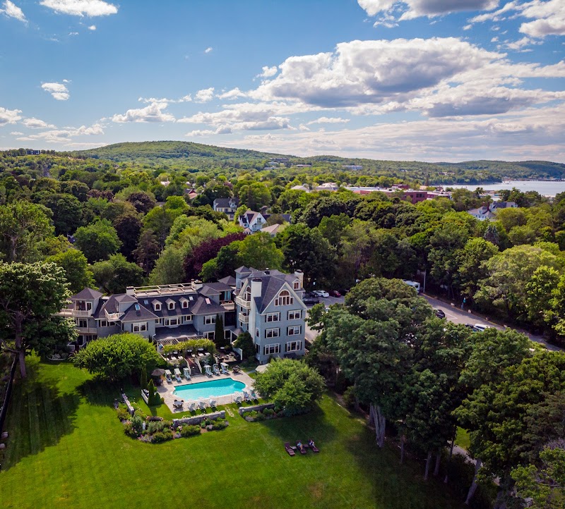 Gray-blue lodge complex with a rectangular pool, lawns, and dense trees in Acadia National Park, with distant shoreline beyond.