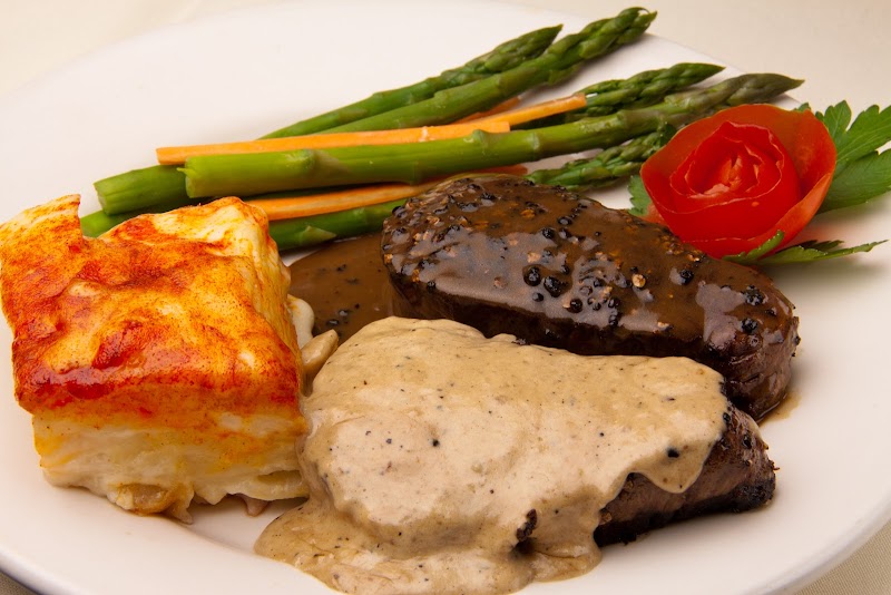 In Acadia National Park, a plated beef tenderloin with peppercorn sauce sits beside asparagus, potato, and a carrot rose on a white plate.