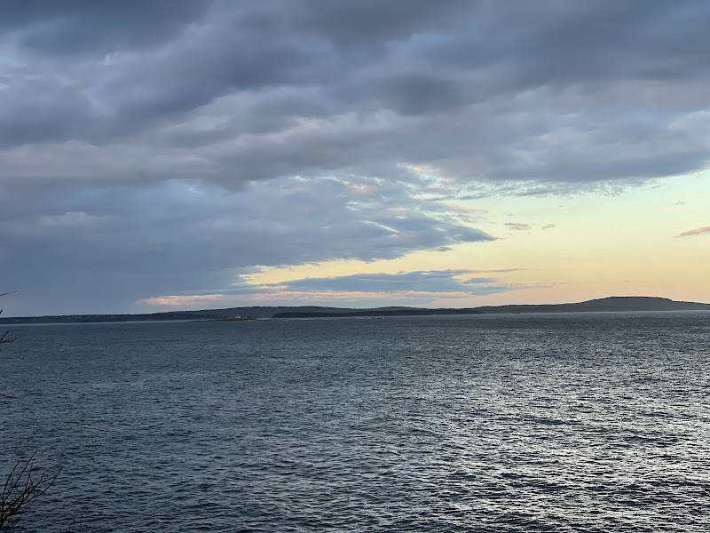 Calm Atlantic water near Acadia National Park coastline at dusk, with rippling waves and a cloudy sky over distant land.
