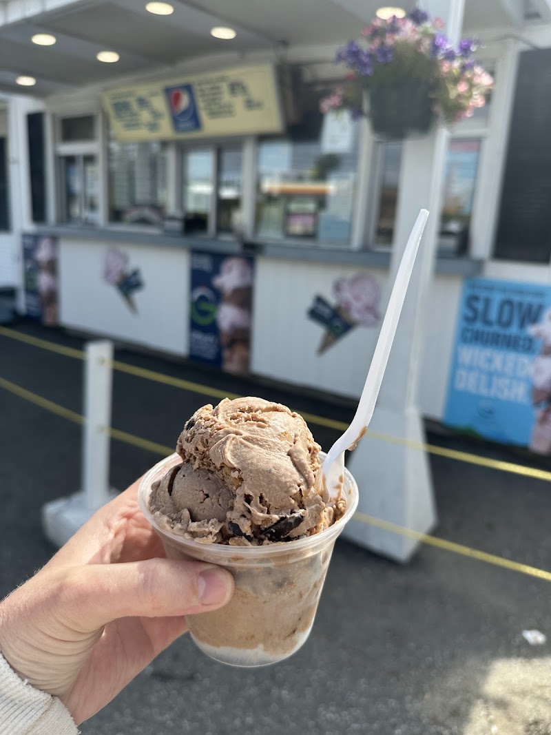 Ice cream cone held up in front of a dairy bar in Acadia National Park, with signs and order window in the background.