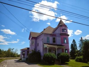 Bright purple Victorian-style house sits beside a rural road in Acadia National Park under a clear blue sky.